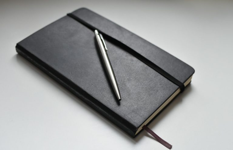 Un carnet noir fermé avec un stylo métallique posé dessus.